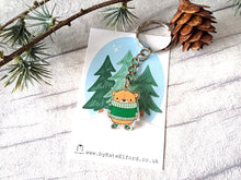 Load image into Gallery viewer, Recycled acrylic brown bear keyring. The bear is wearing a big green jumper which sits just under his nose, so he looks very snug, and he is wearing matching green stripey socks. Displayed on a white mini tree backing card
