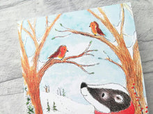 Load image into Gallery viewer, A close up of a notebook. It shows a badger looking up at two robins sat in the trees, it is an A6 notebook