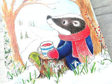 Load image into Gallery viewer, A close up of a notebook. A badger sat drinking a cup of tea sat in the snow with snowdrops