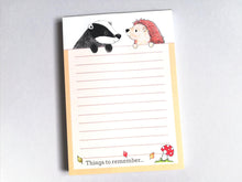 Load image into Gallery viewer, Hedgehog and badger notepad, A6 note pad. It is a orangey golden colour around the border. There is a little red toadstool at the bottom with the wording things to remember