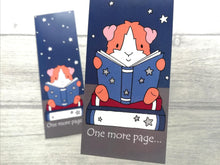 Load image into Gallery viewer, Close up of a guinea pig bookmark. The guinea pig is sat on a book reading another book. It is a ginger and white guinea pig. The wording on the bottom of the bookmark is one more page