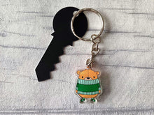 Load image into Gallery viewer, Recycled acrylic brown bear keyring. The bear is wearing a big green jumper which sits just under his nose and he is wearing matching green stripey socks. It is around 3cm tall