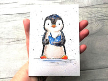 Load image into Gallery viewer, An A6 size notebook with a penguin painting design on the cover, held in a hand as a size guide