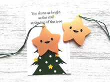 Load image into Gallery viewer, Small gold colour acrylic star tree decorations with happy faces. The backing card is a picture of the top of a Christmas tree and the wording says you shine as bright as the star at the top of the tree