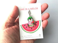 Load image into Gallery viewer, Mini penguin keyring, made from recycled acrylic. A little penguin holding a slice of watermelon wearing a watermelon jumper and hat. The wording on the backing card reads you are one in a melon. It is being held in a hand in the photo as a size guide
