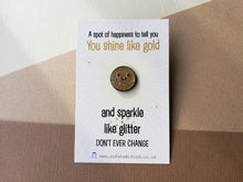 Load image into Gallery viewer, A miniature round gold and sparkly glitter enamel pin with a happy face. It is on a small rectangular backing card which has the wording a spot of happiness to tell you you shine like gold and sparkle like glitter. Don't ever change. Designed by Kate Elford