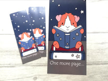 Load image into Gallery viewer, Guinea pig bookmark. The guinea pig is sat on a book reading and the the words at the bottom of the bookmark reads one more page
