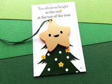 Load image into Gallery viewer, Smiling acrylic star decoration with a happy face. It is a metallic gold colour. The backing card is a picture of the top of a Christmas tree and the wording says you shine as bright as the star at the top of the tree