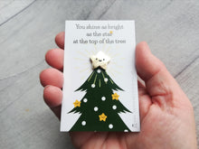 Load image into Gallery viewer, Mini smiling star gold enamel pin. It is displayed on a small rectangular white backing card which has a picture of a green Christmas tree. The wording at the top of the card reads you shine as bright as the star at the top of the tree. Shown in a hand in the photo to show how small it is