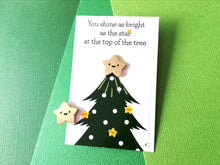 Load image into Gallery viewer, Little happy gold star enamel pin. It is displayed on a small rectangular backing card which has a picture of a Christmas tree. The wording at the top of the card reads you shine as bright as the star at the top of the tree