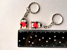 Load image into Gallery viewer, Two little recycled penguin keyrings holding red smiley face hearts. They are next to a ruler to show the size.