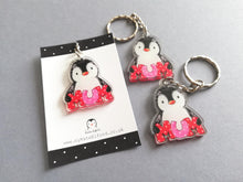 Load image into Gallery viewer, Mum penguin keyrings. The penguins are holding the word mum in big red and pink polka dot letters. Made from recycled acrylic and displayed on a small black and white card. It is the same design on both sides of the keyring. It measures around 4cm tall