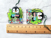 Load image into Gallery viewer, Penguin and house plants recycled acrylic hanger. Shown next to a ruler as a size guide. They measure approximately 5cm tall not including the thread.