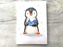 Load image into Gallery viewer, A penguin writing in a notebook. The design is printed on an A6 lined notebook