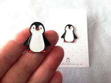 Load image into Gallery viewer, Black and white penguin enamel pin on a grey and white polka dot backing card. There is a hand in the photo holding a pin to show how small it is