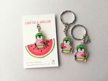 Load image into Gallery viewer, Mini penguin recycled acrylic keyrings.
The design is a penguin holding a slice of watermelon, dressed in a pink, yellow and green watermelon jumper and a watermelon hat.
The wording on the white backing card reads you are one in a melon.