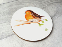 Load image into Gallery viewer, A glossy round white coaster. The image printed on the coaster is a watercolour fluffy robin sat on a branch with a few leaves and one leaf falling. It has a plain white background