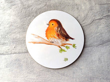 Load image into Gallery viewer, A round glossy robin coaster. The image printed on the coaster is a watercolour fluffy robin sat on a branch with a few leaves and one leaf falling. The background is plain white.