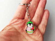 Load image into Gallery viewer, A little penguin keyring, made from recycled acrylic. Penguin is wearing a watermelon jumper, hat and holding a slice of watermelon. It is photographed in a hand to show how small it is