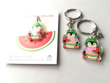 Load image into Gallery viewer, Mini penguin recycled acrylic keyrings. Little penguins holding slices of watermelon, and dressed in a pink, yellow and green watermelon jumper. They are wearing watermelon hats. The wording on the square white backing cards reads you are one in a melon.
