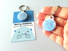 Load image into Gallery viewer, Worry gobbler mini round keyring. Blue cute blob character on a backing card with the words worry gobbler carry me with you wherever you go. Held in a hand to show how small it is