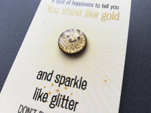 Load image into Gallery viewer, A close up of round gold glitter sparkly mini enamel pin with a simple happy face design. It is on a rectangular backing card which has the wording a spot of happiness to tell you you shine like gold and sparkle like glitter. Don't ever change. Designed by Kate Elford