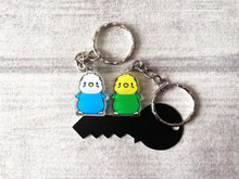 Load image into Gallery viewer, A cute pair of budgies. One is blue and white and the other is green and yellow. They are illustrated acrylic keyrings