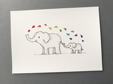 Load image into Gallery viewer, A 7x5 print of a big elephant with a small elephant stood behind holding the elephants tail with its trunk. The big elephant is squirting water above them which is rainbow colour drops