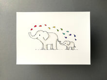 Load image into Gallery viewer, A cute 7x5 print of a bigger elephant with a smaller elephant stood behind holding the elephants tail in it's trunk. The big elephant is squirting water above them which is rainbow colour drops