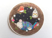 Load image into Gallery viewer, Round vinyl sticker. Mouse is asleep in a tree, with a blanket, cup of tea and some books. There is also a robin, lantern, stars and toadstools
