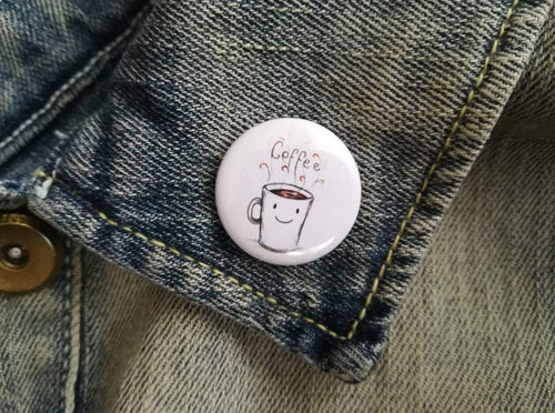 A mini white button badge, the illustration is a happy mug with coffee written in the steam