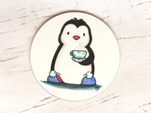 Load image into Gallery viewer, Penguin coaster. A black and white penguin on a white background. Penguin is wearing blue slippers with pom poms on the toes, and is holding a polka dot cup and saucer
