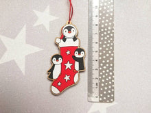 Load image into Gallery viewer, Penguin Christmas stocking decoration. Wooden penguins Christmas tree ornament. Red and white stocking with stars, eco friendly wood