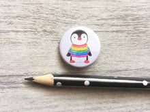 Load image into Gallery viewer, Mini button badge. A small round badge with a white background. The picture is a black and white penguin wearing a rainbow colour striped jumper. It is placed next to a pencil to give a size guide
