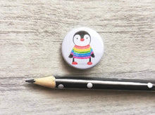 Load image into Gallery viewer, Mini button badge. A small round badge with a white background. The picture is a black and white penguin wearing a rainbow colour striped jumper. It is placed next to a pencil to give a size guide