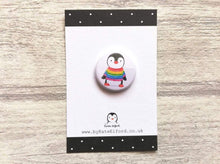 Load image into Gallery viewer, Mini button badge. A small round badge with a white background. The picture is a black and white penguin wearing a rainbow colour striped jumper