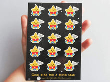 Load image into Gallery viewer, An A6 sticker sheet, with gold star for a super star written on it. There are lots of little star stickers in blue capes and red pants holding a flag saying super