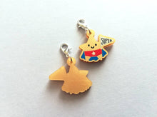Load image into Gallery viewer, Back and front of a gold acrylic star, a gold star for a super star stitch marker. The star has a smile and is wearing a blue cape and red pants, holding a flag saying super
