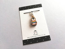 Load image into Gallery viewer, Small wooden stitch marker, little penguin design wearing a rainbow striped jumper. Eco friendly wood