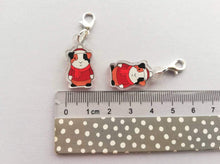 Load image into Gallery viewer, Guinea pigs in clear recycled acrylic wearing red jumper, hat and scarf. The charm has been turned into a stitch marker