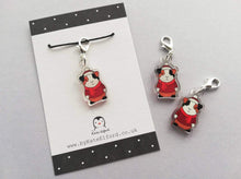 Load image into Gallery viewer, Little clear acrylic guinea pig stitch marker. It is made from recycled acrylic, the guinea pig is wearing a red hat, jumper and scarf by Kate Elford