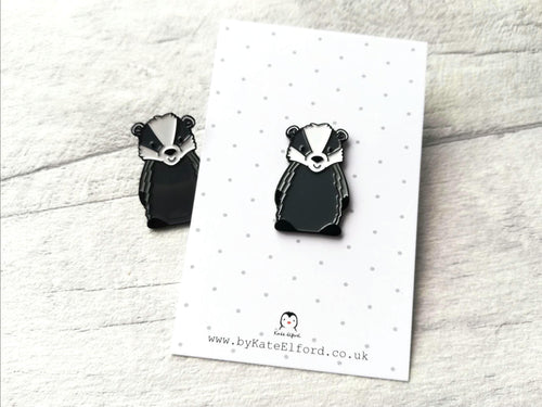 A cute badger enamel pin on a backing card with a little badger peeking out from behind the card