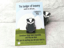 Load image into Gallery viewer, A badger enamel pin on a mini backing card, with a badger peeking out from behind. The backing card has the wording the badger of bravery wants to tell you I believe in you. Sometimes things seem impossible until they are done. You can do anything you set your mind to
