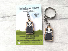 Load image into Gallery viewer, A cute miniature wooden badger keyring displayed on a backing card. The backing card has the wording the badger of bravery wants to tell you I believe in you. Sometimes things seem impossible until they are done. You can do anything you set your mind to
