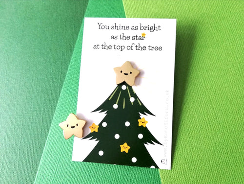 Little happy gold star enamel pin. It is displayed on a small rectangular backing card which has a picture of a Christmas tree. The wording at the top of the card reads you shine as bright as the star at the top of the tree