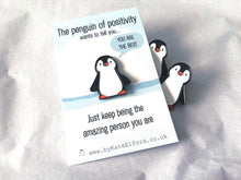 Load image into Gallery viewer, A little penguin enamel pin on a backing card with the wording the penguin of positivity wants to tell you, you are the best. Just keep being the amazing person you are. There are a couple of penguins peeking out from behind the card

