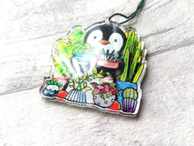 Load image into Gallery viewer, Penguin and house plants recycled acrylic hanger. Shown at an angle so the light reflects showing the reflection of how smooth and glossy it is
