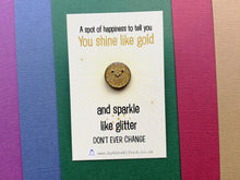 Load image into Gallery viewer, A mini round gold glittery enamel pin with a happy face. It is on a small white and gold colour backing card which has the wording a spot of happiness to tell you you shine like gold and sparkle like glitter. Don&#39;t ever change. Designed by Kate Elford
