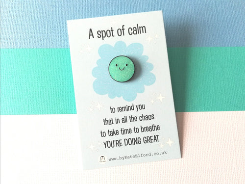 A spot of calm enamel pin. A cute blue glittery round pin with a happy face. The wording on the card says A spot of calm to remind you that in all the chaos to take time to breathe you're doing great