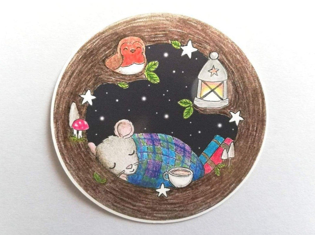 Round vinyl sticker. Mouse is asleep in a tree, with a blanket, cup of tea and some books. There is also a robin, lantern, stars and toadstools